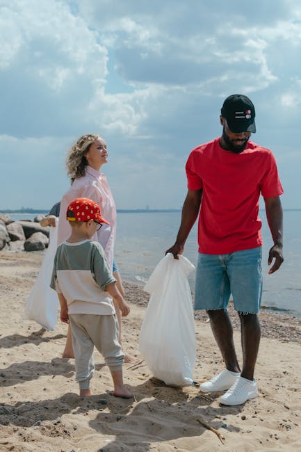 A man wearing a red T-shirt, denim shorts, white sneakers, and a black cap with a small British flag detail is standing on a sandy beach, holding a large white rubbish bag in his right hand with a foc